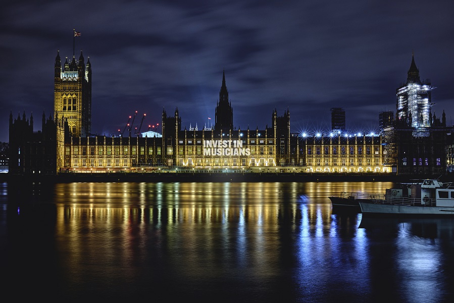 Photograph of the houses of parliament at night, with a light projection shone on it with the words 
