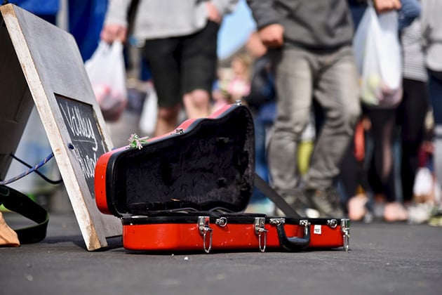 Red guitar case on street open for donations to busker, crowd out of focus in background