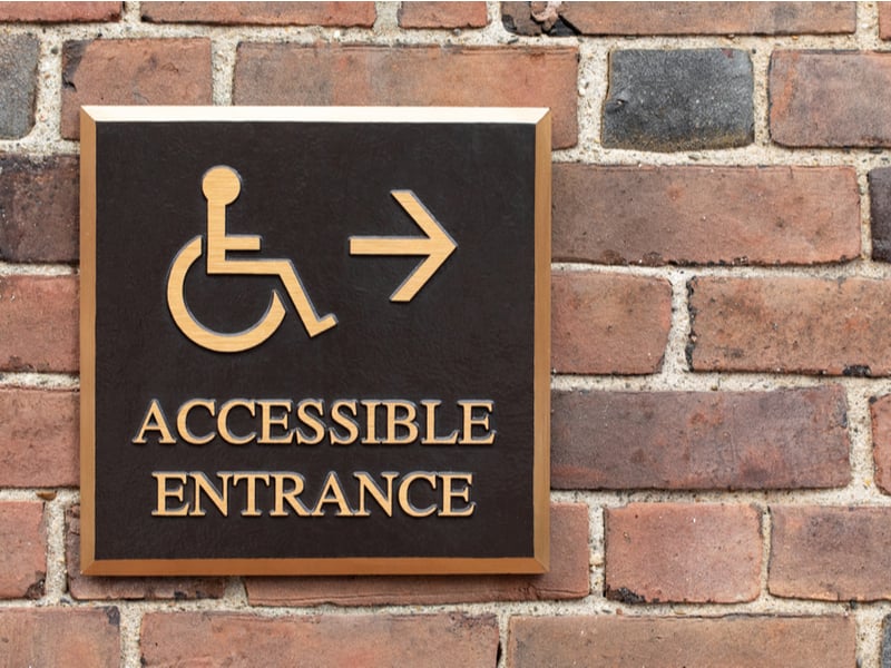 Photograph of an accessible entrance sign attached to a brick wall outside a building.