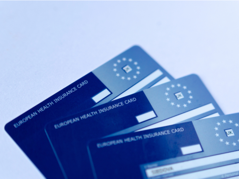 Three of the familiar, blue plastic European Health Insurance Cards stacked against a pale blue background
