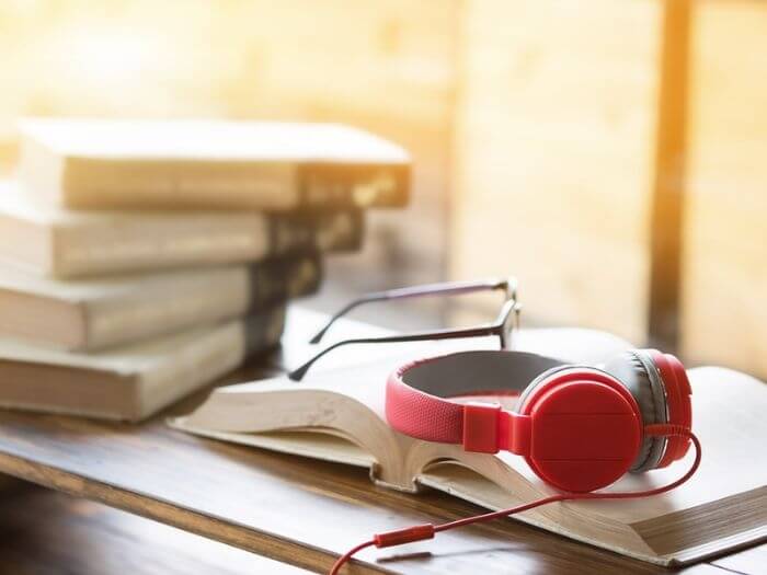 Red headphones on an open book with pair of glasses.