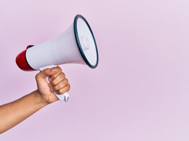 A hand holding a white megaphone in front of a pink background.