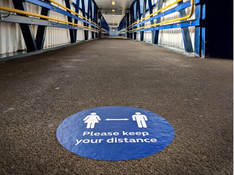 A blue sticker on the floor of a bridge above a train station, the sticker reads 