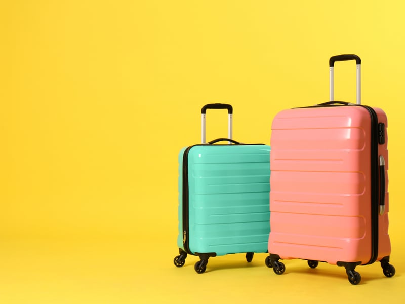 Photograph of two colourful suitcases against a bright yellow background.