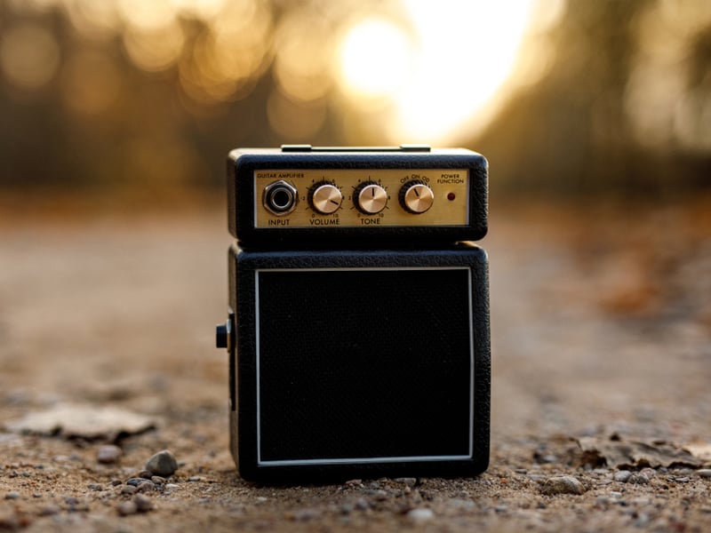 A tiny guitar amp sits on sand with the sun setting behind it.