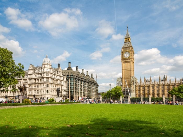Photograph of Parliament square in the sunshine, the photograph looks across the square towards the houses of parliament and the grass is green.