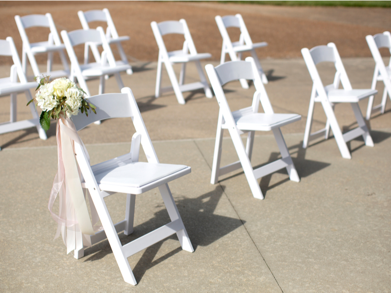 White painted chairs set out with socially distanced amount of space between them, outdoors.